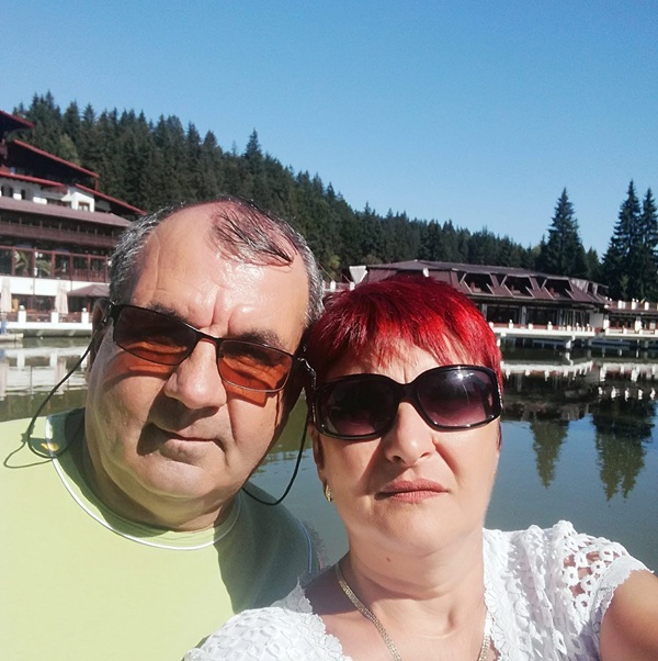 femeie roscata tunsa scurt cu ochelari de soare imbracata in alb face un selfie cu sotul ei imbracat in verde