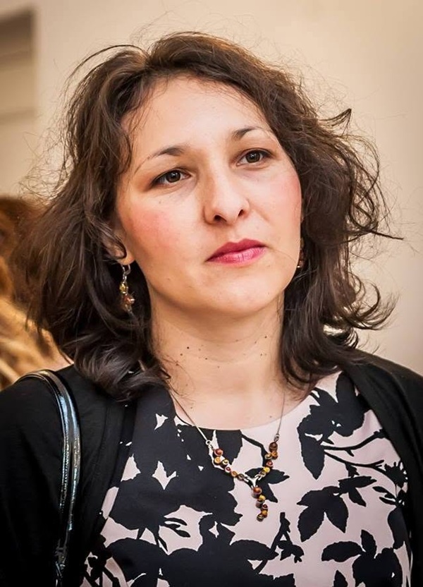 profesoara cu parul ondulat imbracata in bluza cu model floral priveste in zare