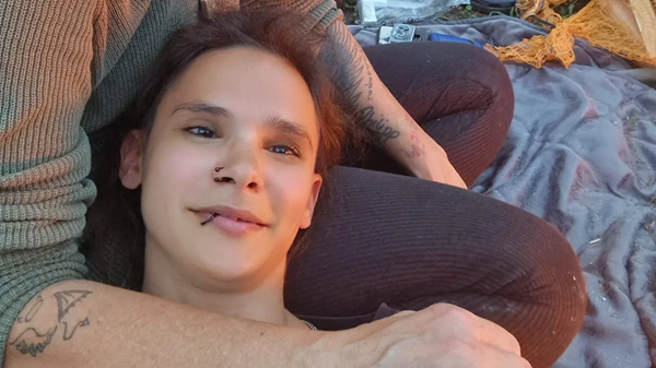 femeie cu cercel in nas sta in bratele unei persoane cu capul si zambeste la camera