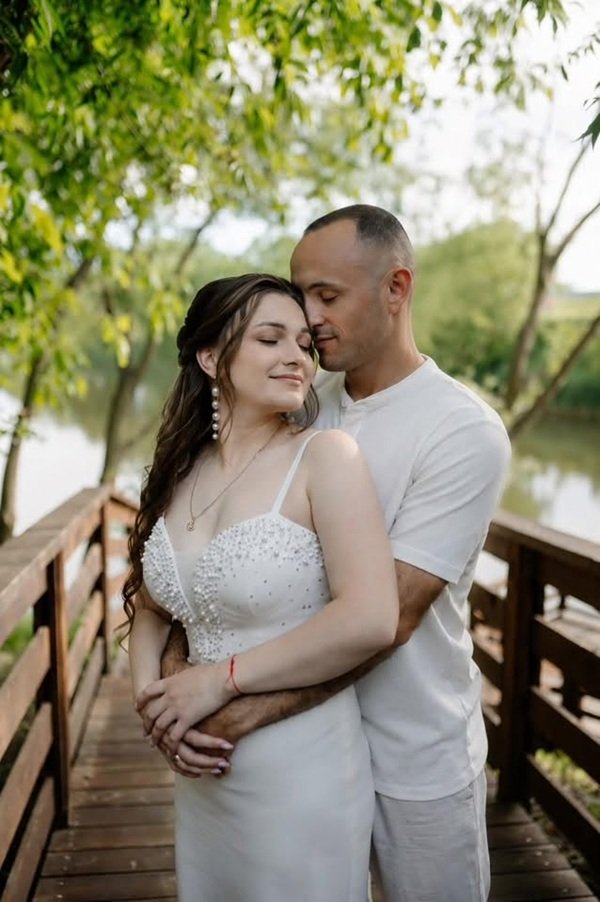barbat imbracat in alb tine in brate o femeie bruneta cu parul lung imbracata in alb pe un pod