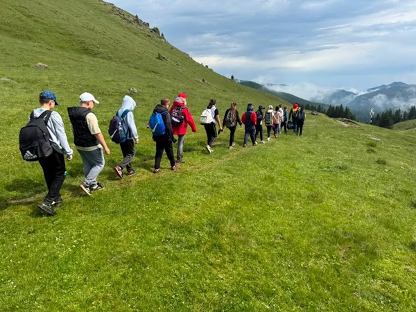 mai multi copii merg aliniati pe munte spre o stana
