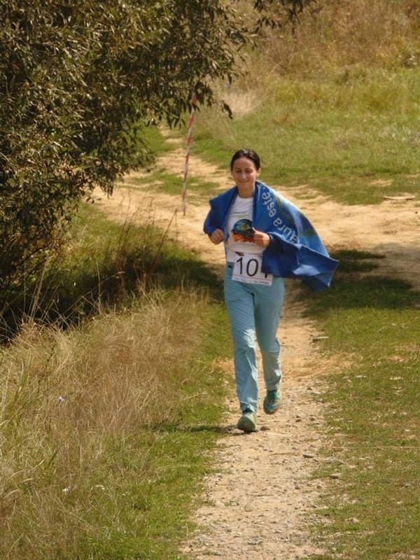 ana oros in blugi si tricou alb alearga pe un teren pe o poteca