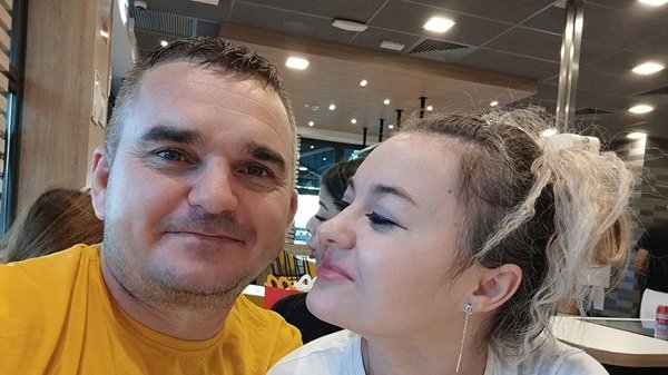 femeie blonda cu parul prins imbracata in alb se uita la un barbat imbracat in galben stau la o masa