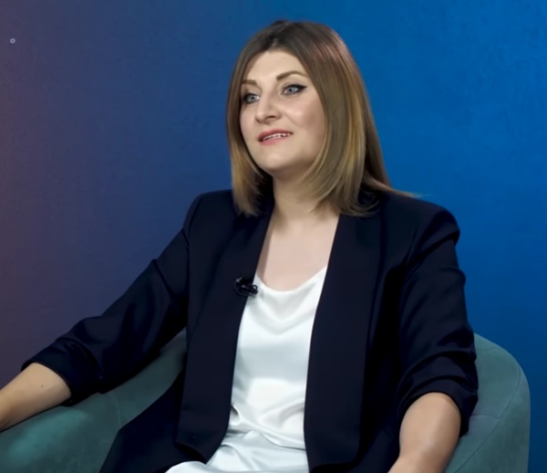 femeie satena in bluza alba si sacou negru pe fundal albastru