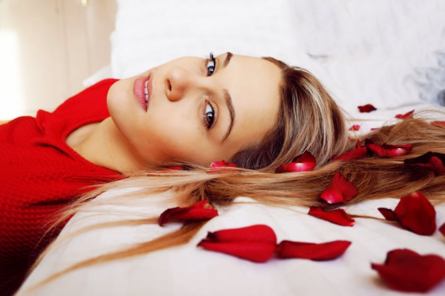 femeie intinsa pe pat cu petale de trandafiri