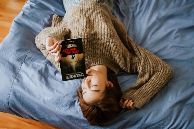 femeie care sta pe pat cu o carte in mana