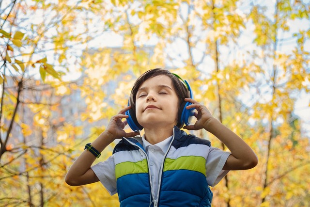 Băiat aflat în natură care ascultă muzică cu căștile la urechi