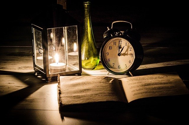 Un ceas, lumânare și carte pe o masă