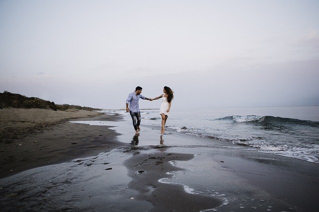 Bărbat și femeie care se țin de mână și aleargă pe malul mării