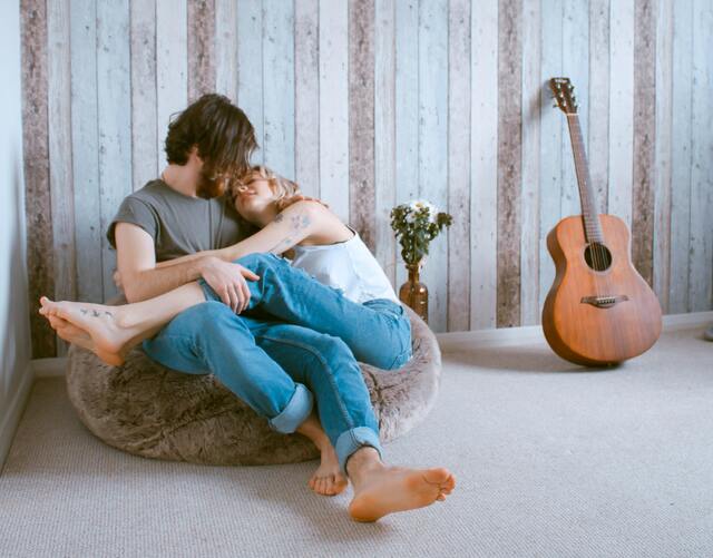 Cuplu de îndrăgostiți așezați pe un fotoliu puf și o chitară lângă ei