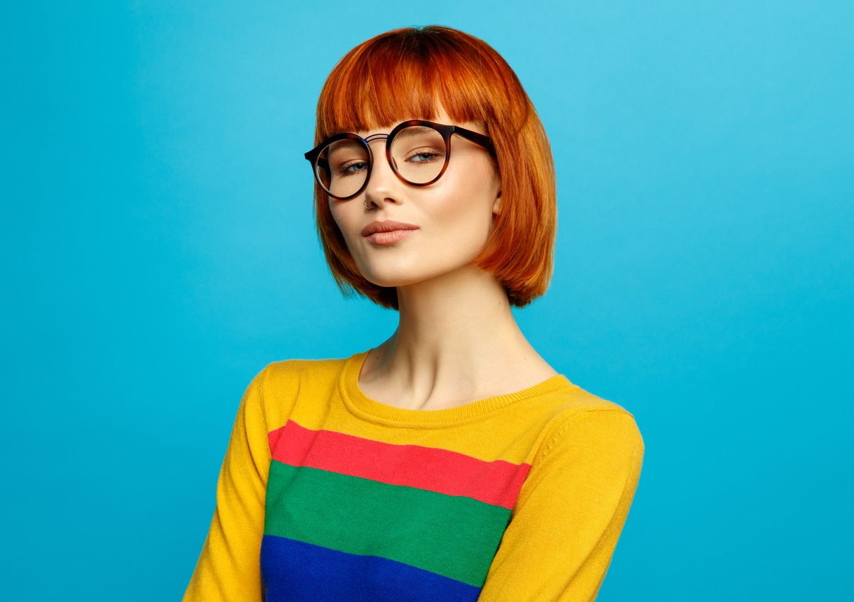 Femeie roscata tunsa scurt cu breton, ochelari si imbracata foarte colorat