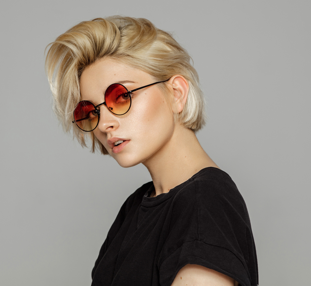 Femeie blondă tunsă scurt cu cărare într-o parte și ochelari de soare