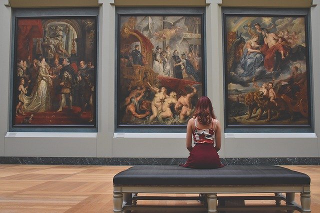 Femeie care stă pe bancă în muzeu și admiră picturi