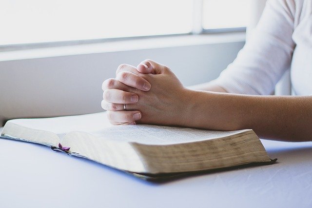Femeie cu mâinile împreunate a rugăciune pe o carte