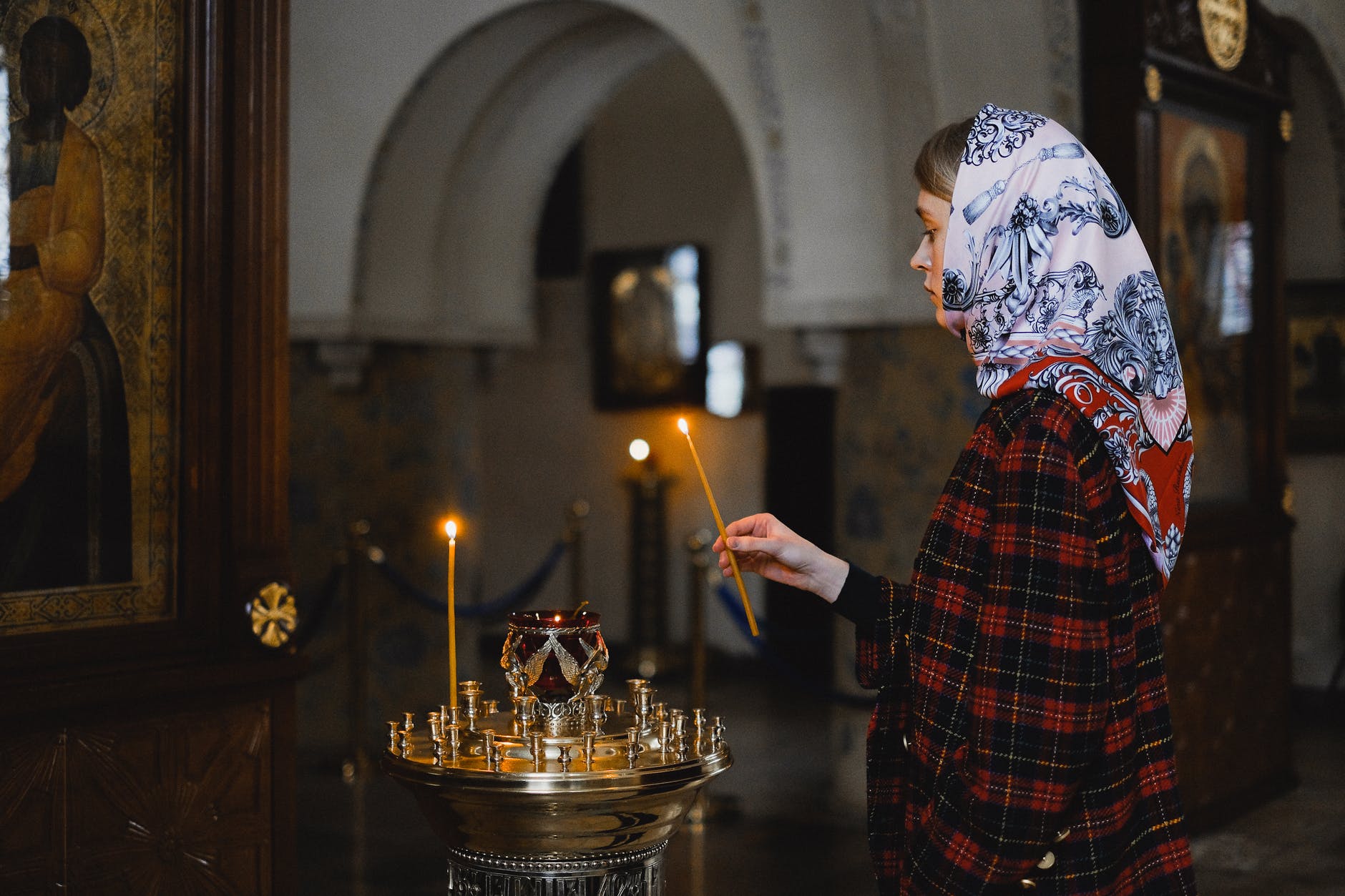 Femeie cu batic care aprinde o lumânare în biserică