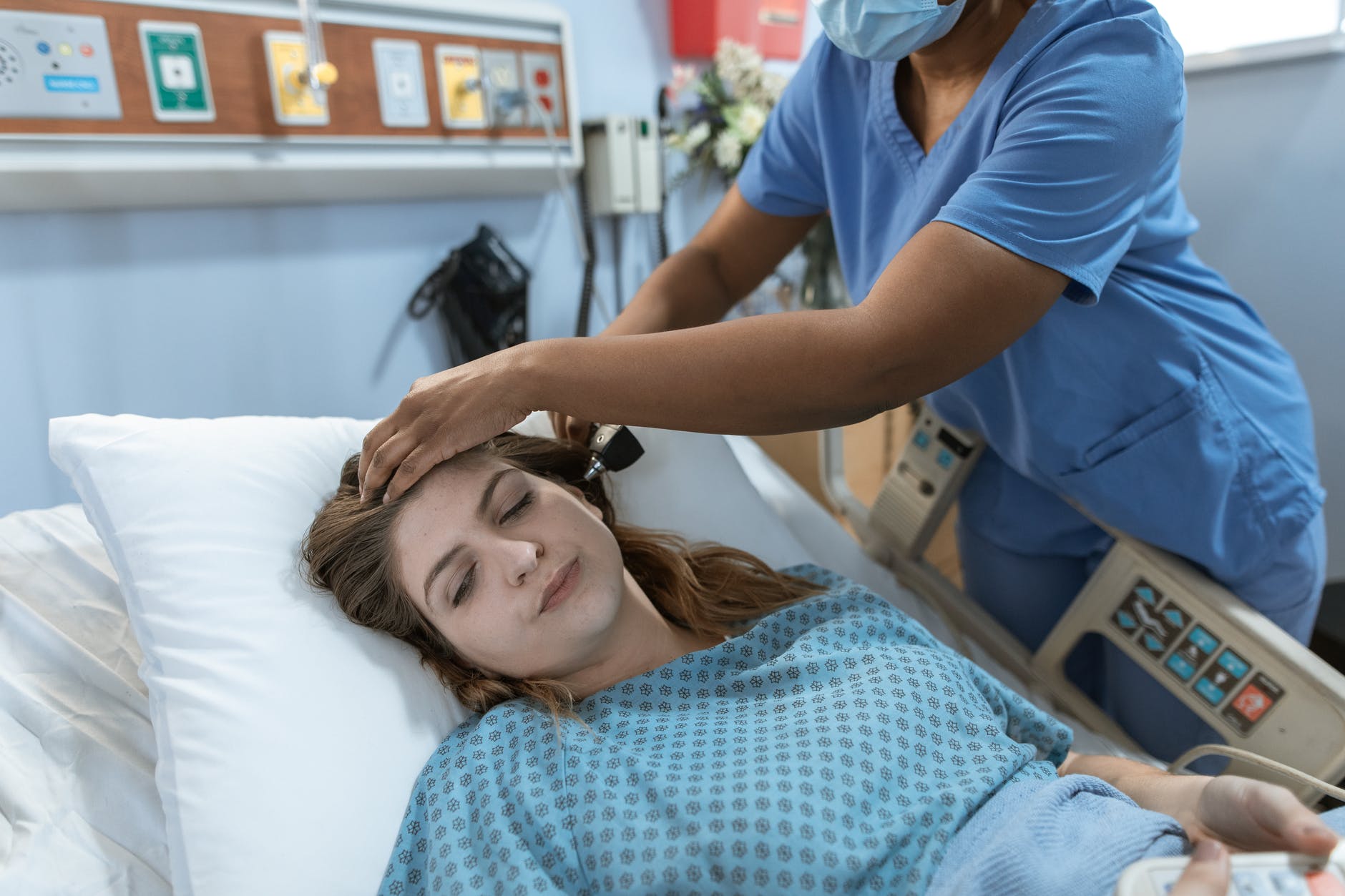 Femeie bolnavă care stă pe un pat de spital și asistentă medicală care-i ia temperatura