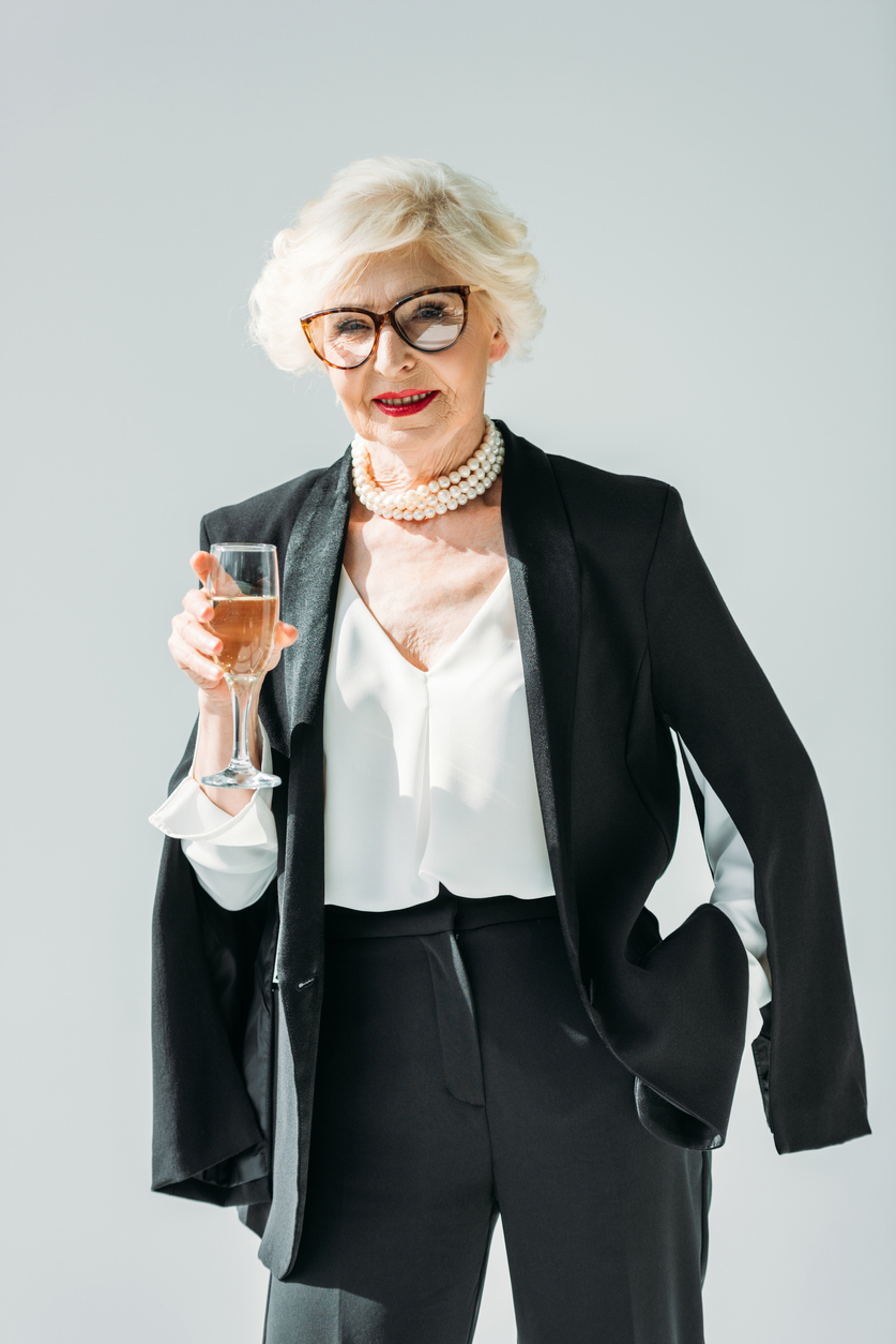 Femeie elegantă îmbrăcată la costum cu un pahar de șampanie în mână