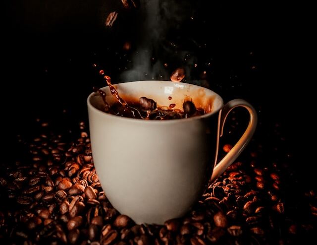 Cană albă cu cafea aburindă pe fundal negru