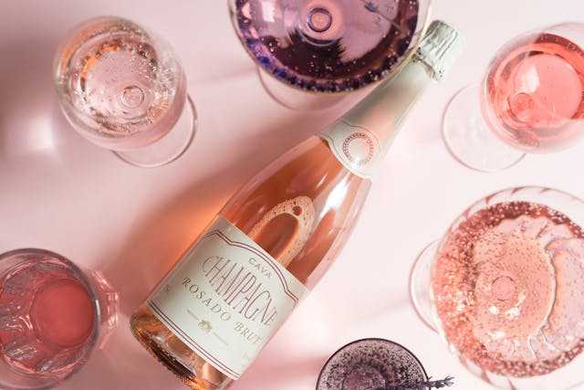 Sticlă de vin spumant roze cu mai multe pahare în jur