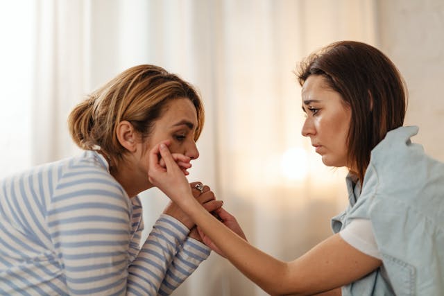 O femeie care plânge și alta care o consolează