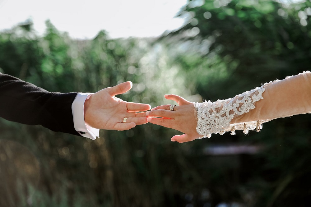 Tineri căsătoriți care își ating mâinile în ziua nunții