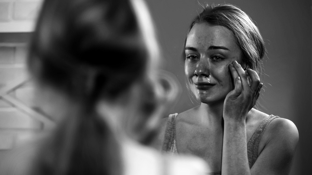Femeie care plânge în oglindă pentru că este nemulțumită de propria imagine