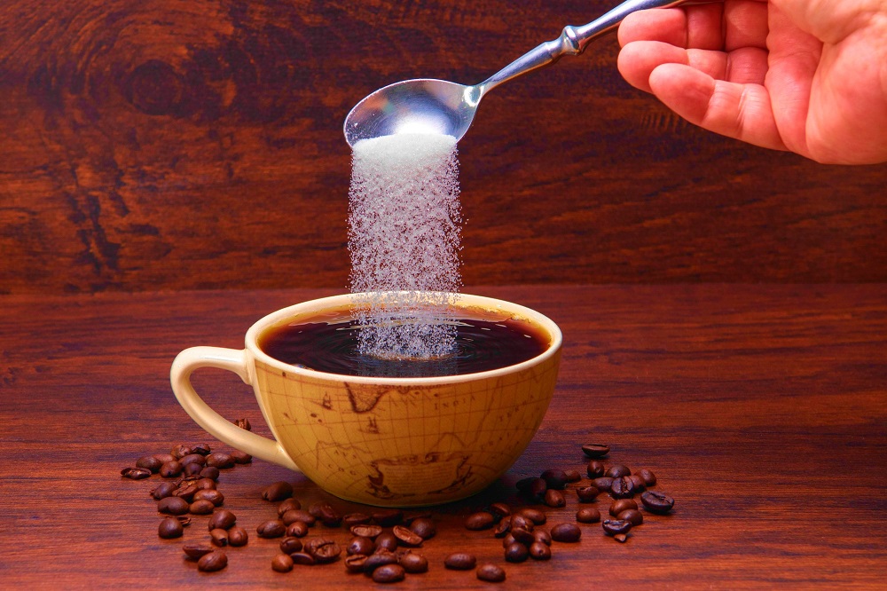 Gestul de a adăuga bicarbonat de sodiu într-o ceașcă de cafea cu desene care imită Globul Pământesc, înconjurată de boabe de cafea