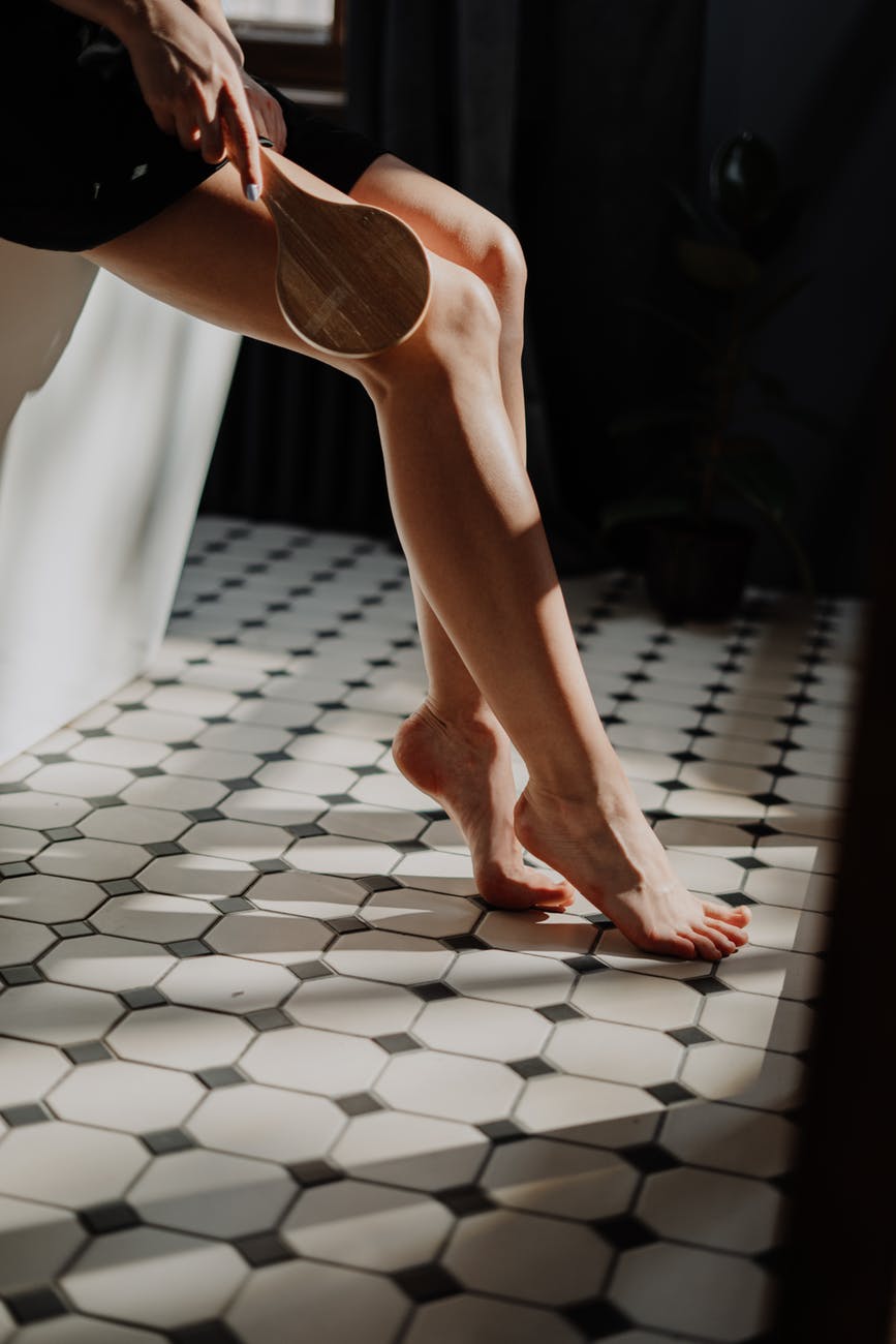 Persoană care își masează picioarele cu o perie, stând pe cada din baie, în timpul rutinei de îngrijire