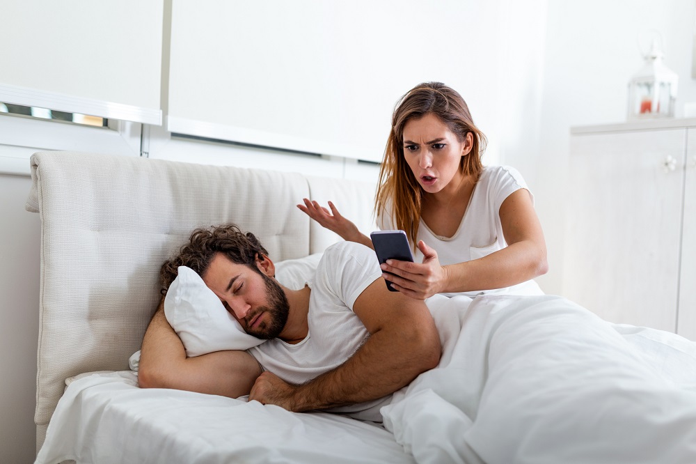 Soție geloasă care verifică telefonul soțului în timp ce el doarme.