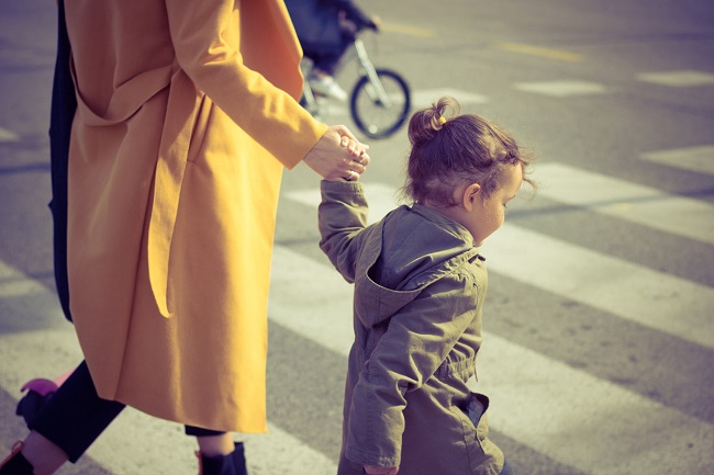 Mamă care traversează strada cu fiica ei de mână.