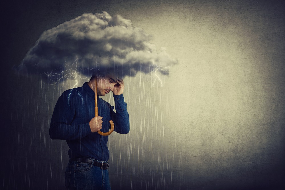 Bărbat pesimist, care stă în ploaie și deși ține o umbrelă în mână, simte că are ghinion mereu și picăturile tot îl udă