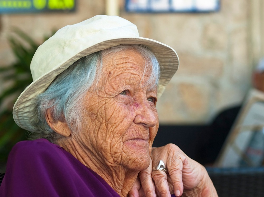Portret de bunică în vârstă, care stă gânditoare și poartă o pălărie pe cap