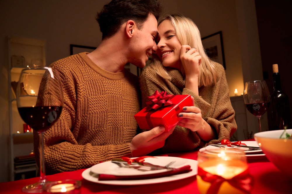 Bărbat care își surprinde partenera cu un cadou de Ziua Îndrăgostiților, în cadrul unei cine romanice.
