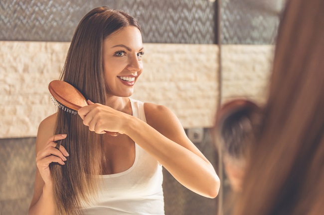 Femeie fericită care se uită în oglindă și își periază părul lung, sănătos și strălucitor