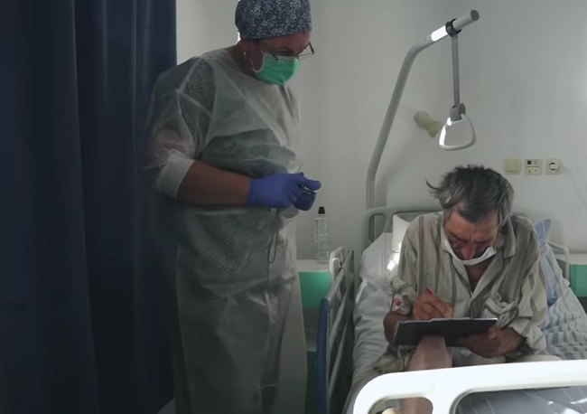Bărbat fără adăpost care a ajuns la spital într-o zi friguroasă de iarnă, surprins în timp ce este ajutat de o asistentă să semneze fișa medicală