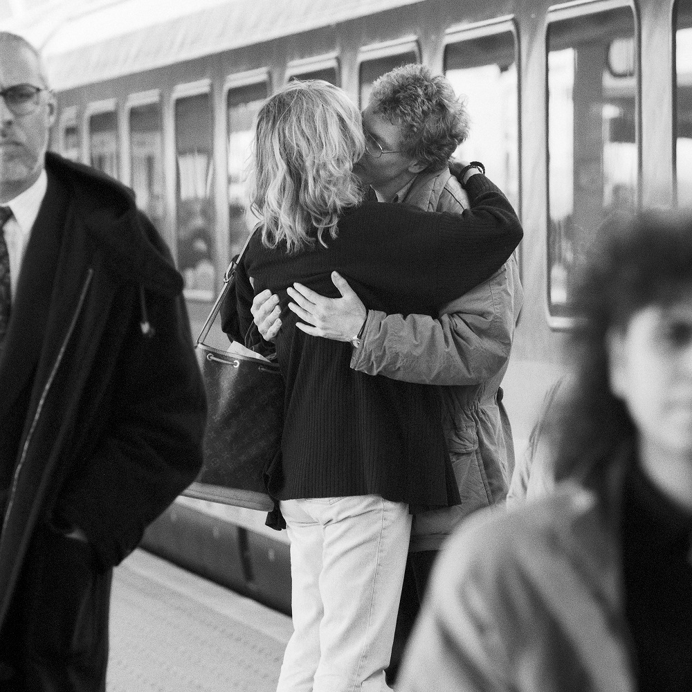 Cuplu îmbrățișat care își ia rămas bun în gară, atunci când unul dintre parteneri trebuie să plece departe.
