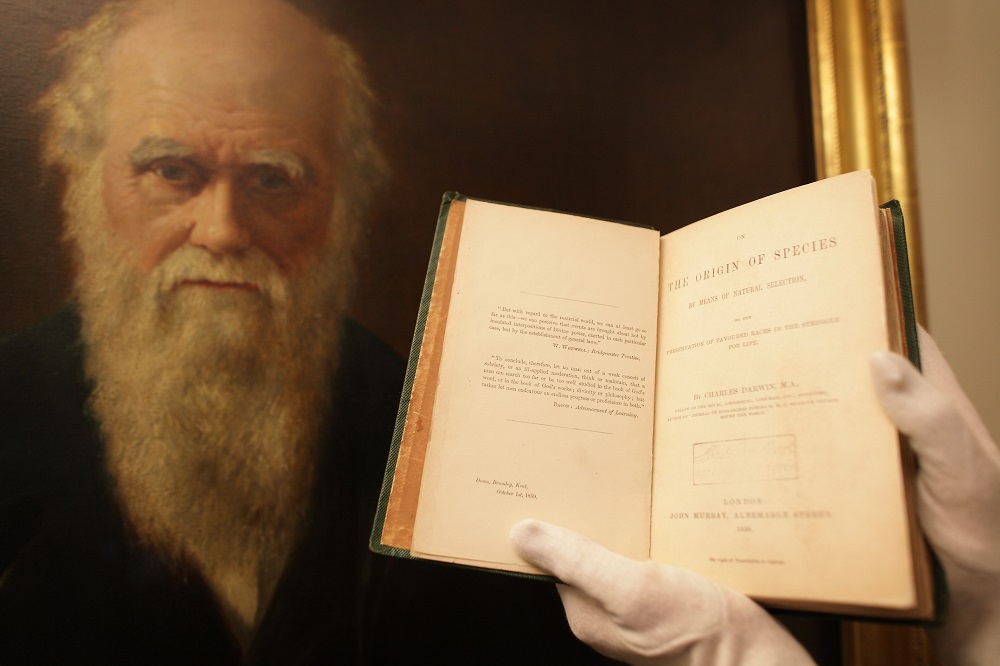 O copie originală a lucrării „Originea speciilor” care face parte din expoziția „The Royal Society: 350 Years of Science”, expusă în fața unui portret al lui Charles Darwin, pe 2 iunie 2010 la Londra, Anglia.