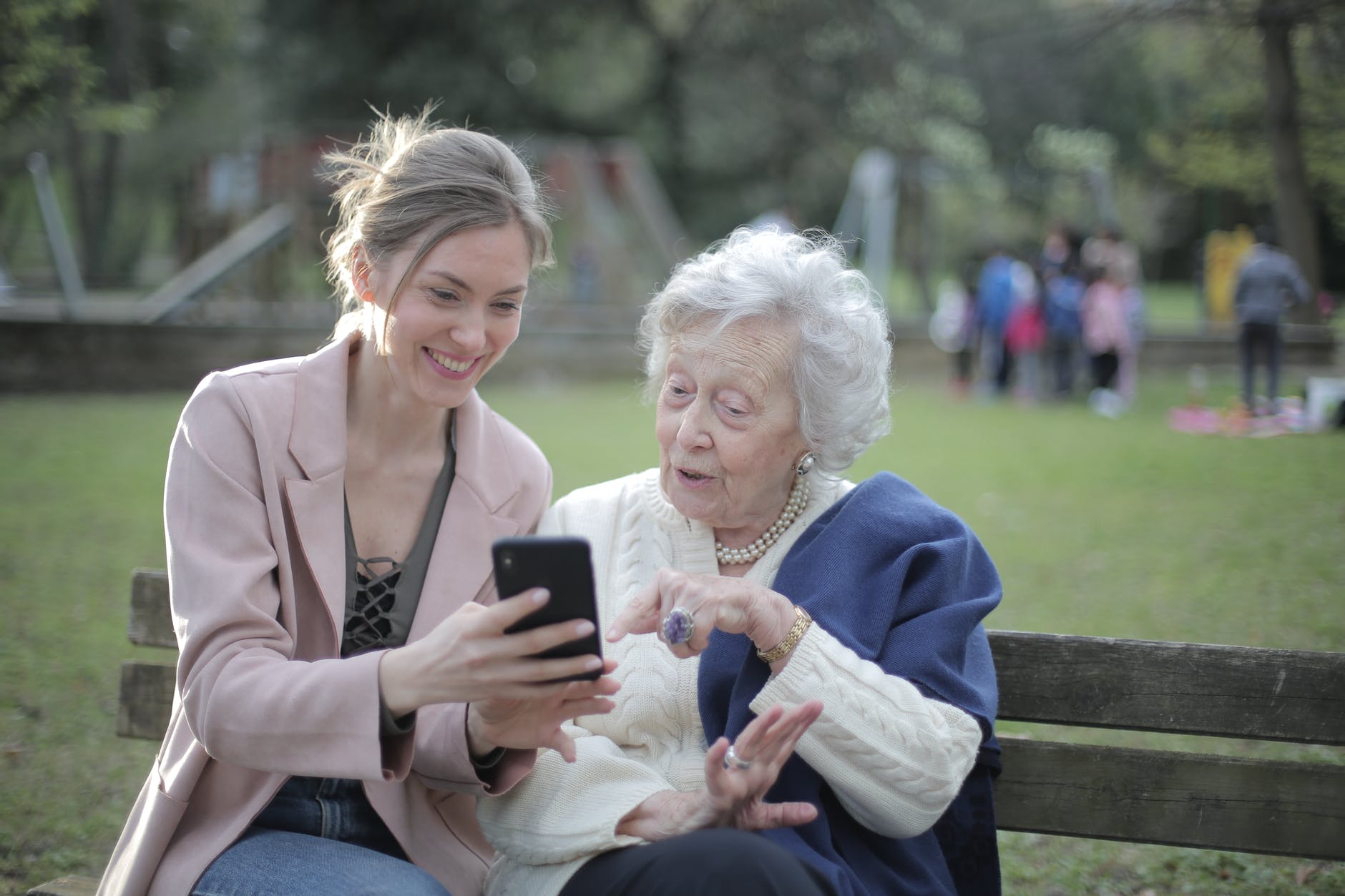 Bunică fericită care butonează un telefon alături de o femeie tânără și este încântată de tehnologie