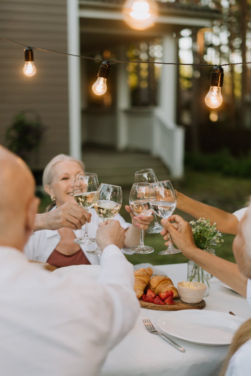 Oameni în vârstă care ciocnesc paharele cu vin alb la o petrecere.