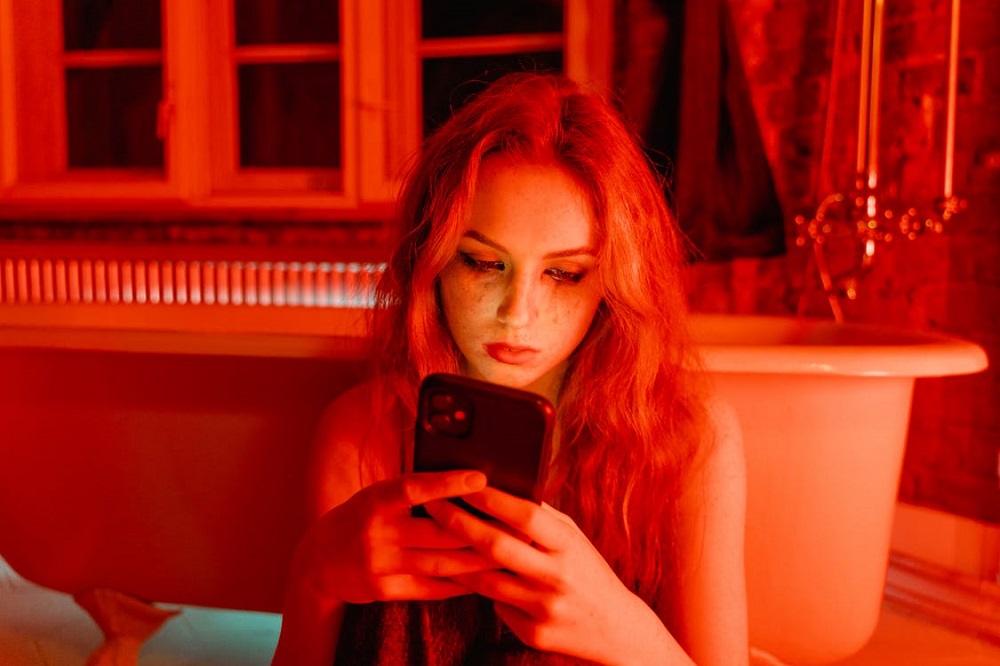 Femeie tristă, cu machiajul curs pe sub ochi, stând cu telefonul în mână, în timp ce așteaptă un semn de la bărbatul pe care îl iubește