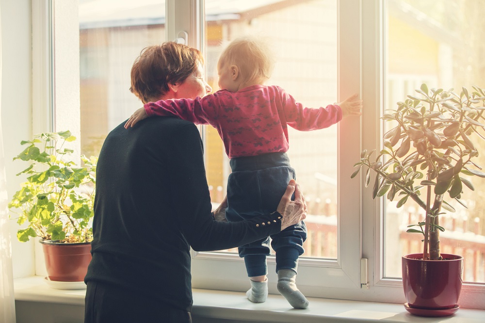 Bunică jucându-se cu nepotul ei lângă fereastră, în timp ce are grijă de acesta