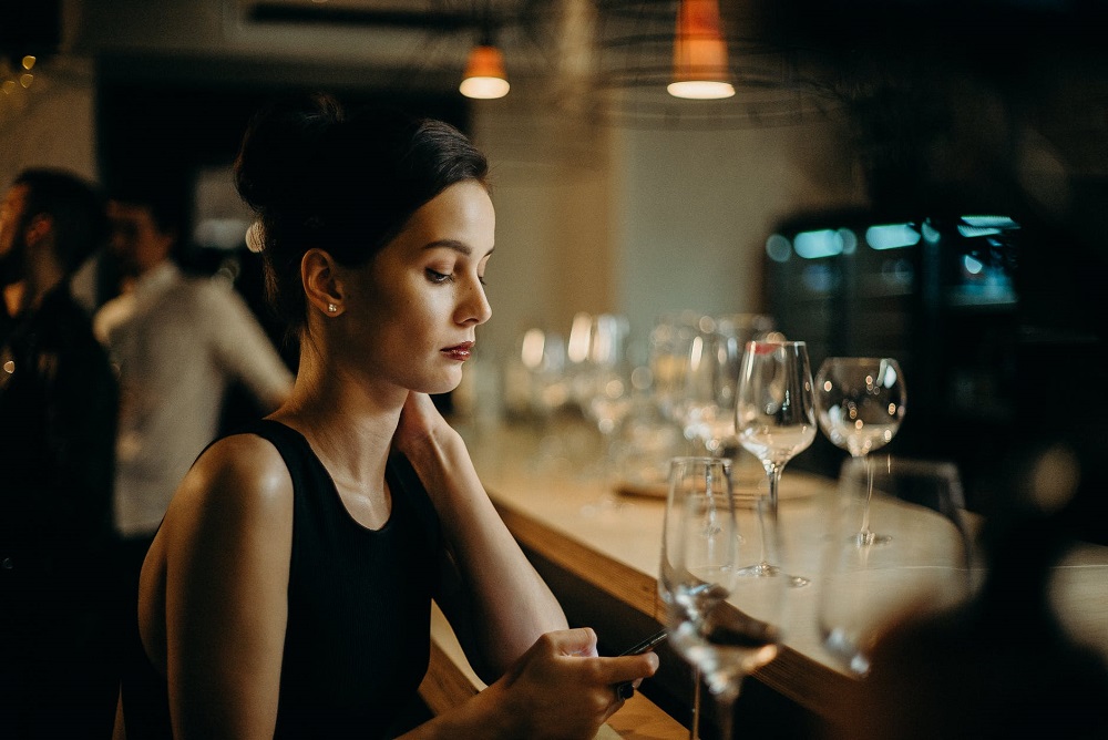 Femeie care stă singură într-un bar și se uită pe telefon