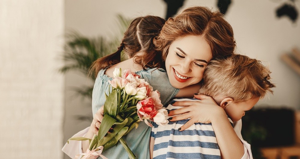 Frați care oferă mamei un buchet de flori, iar ea îi îmbrățișează.
