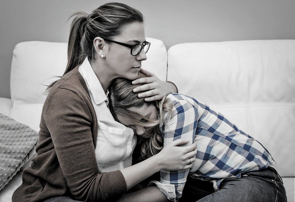 Mamă care își îmbrățișează fiica supărată, încercând să o calmeze