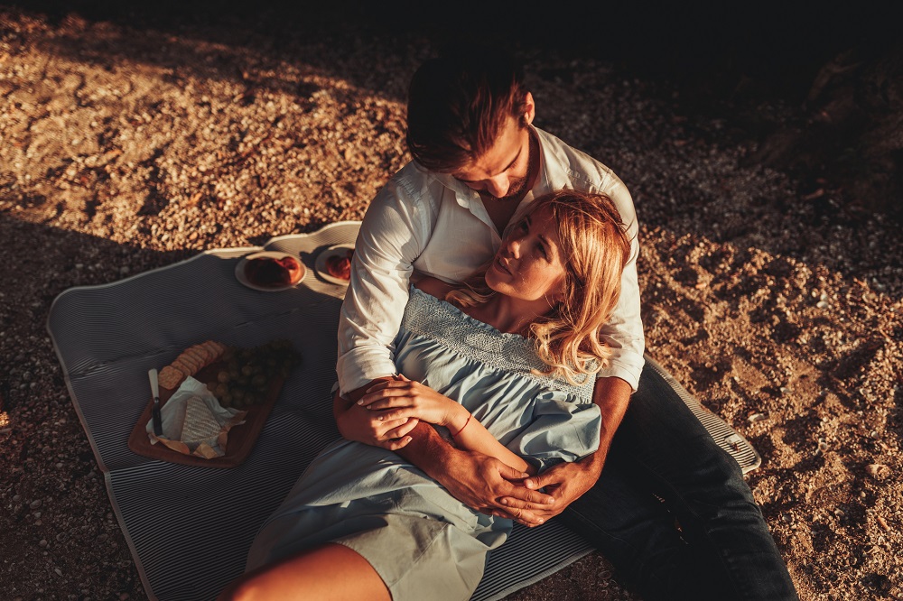 Cuplu îndrăgostit și îmbrățișat, la un picnic pe plajă.