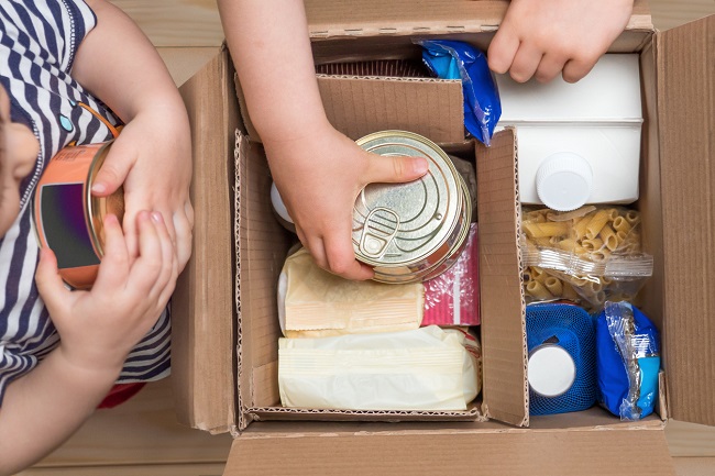 Copii care ambalează o cutie cu donații, alimente neperisabile, pentru cei aflați în nevoie. 