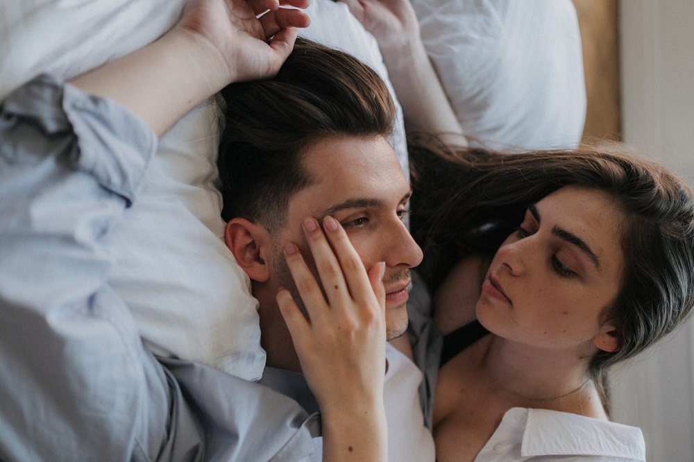 Imagine care ilustrează intimitatea de cuplu, femeia își privește partenerul, în timp ce stau amândoi în pat.