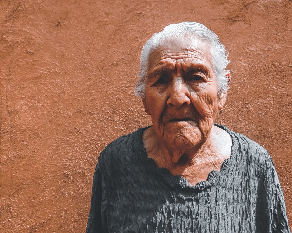 Femeie în vârstă care stă lângă un zid maro