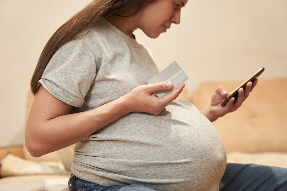 Femeie însărcinată care butonează telefonul și încearcă să efectueze o plată online.