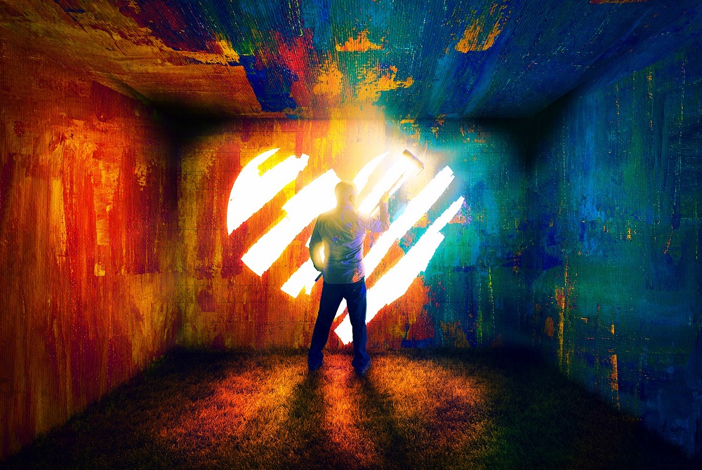 Un bărbat pictează o inimă în lumina razelor care pătrund în întunericul unei încăperi.